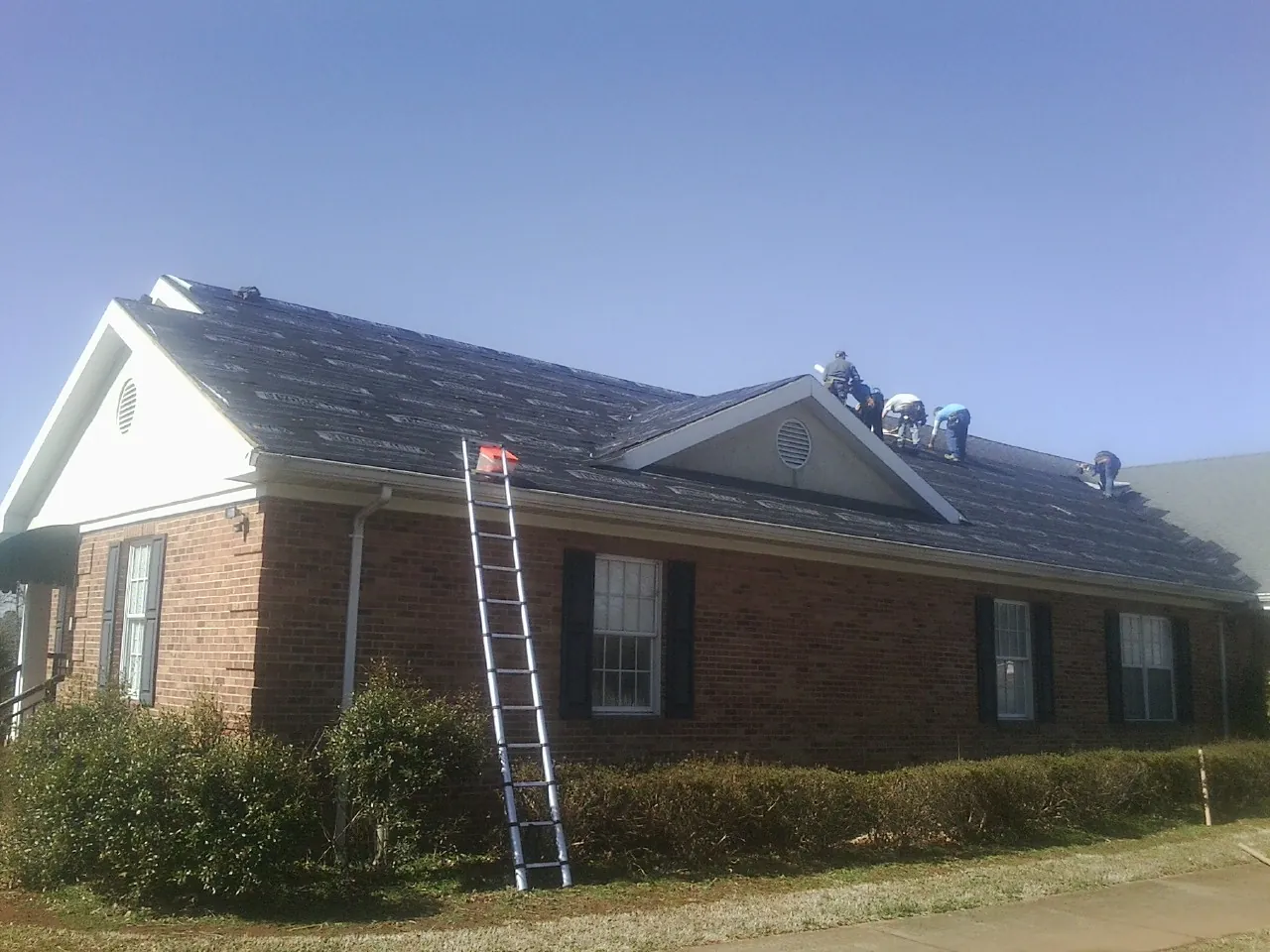 Crew tearing shingles off a brick ranch roof with a ladder set — Metal Roof Repair work by our crew in Fort Ransom