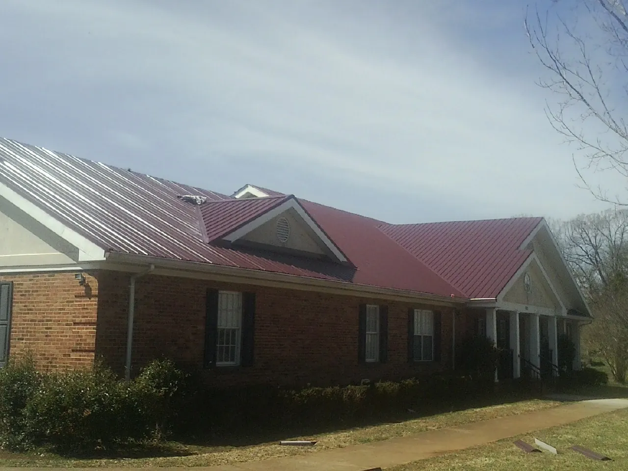 Red metal roof with gabled entries on a long brick building, from a Hail Damage Roof Repair job in Fort Ransom