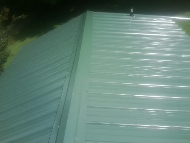New green metal panels meeting at the ridge of a roof — Flat Roof Repair work by our crew in Fort Ransom