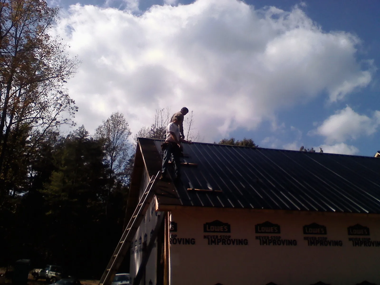 Roofer fastening dark metal panels high against a cloudy sky, from a Roof Inspection job in Fort Ransom