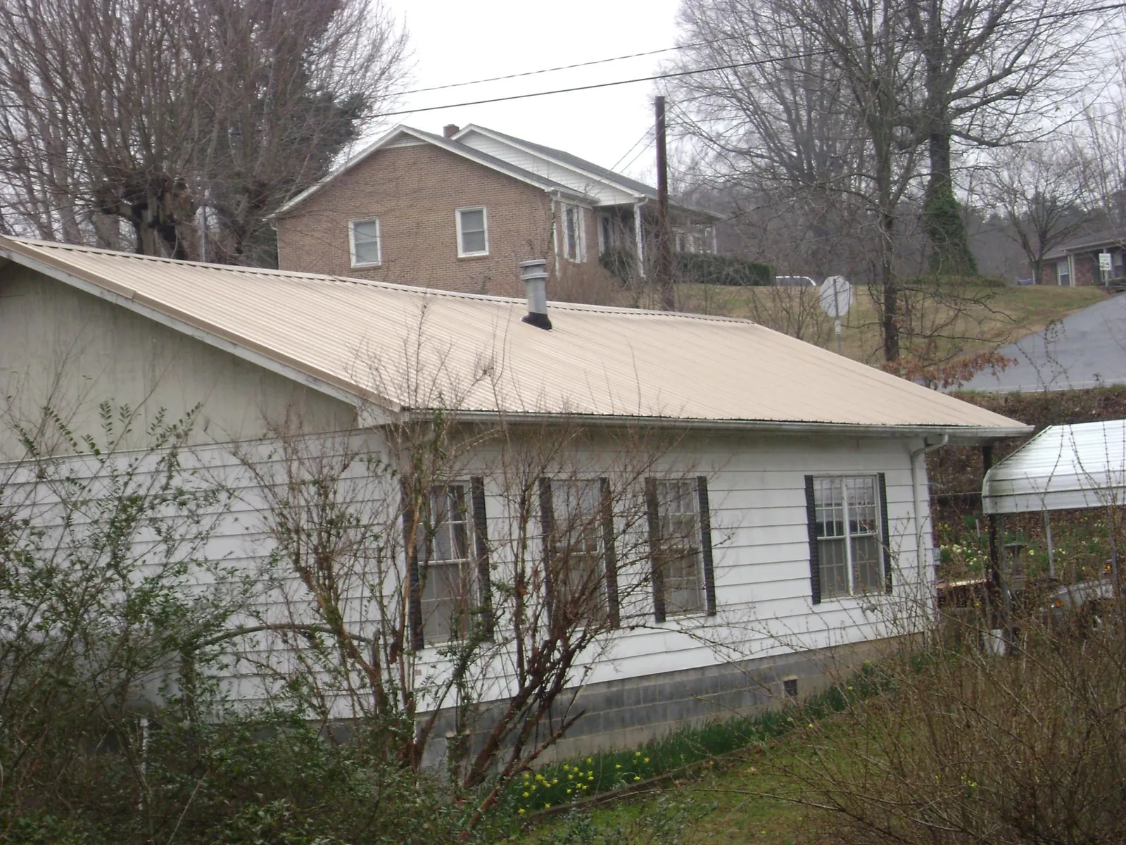 Tan metal roof on a white sided house set into a hillside — Commercial Roofing by Roofing Brothers in Fort Ransom