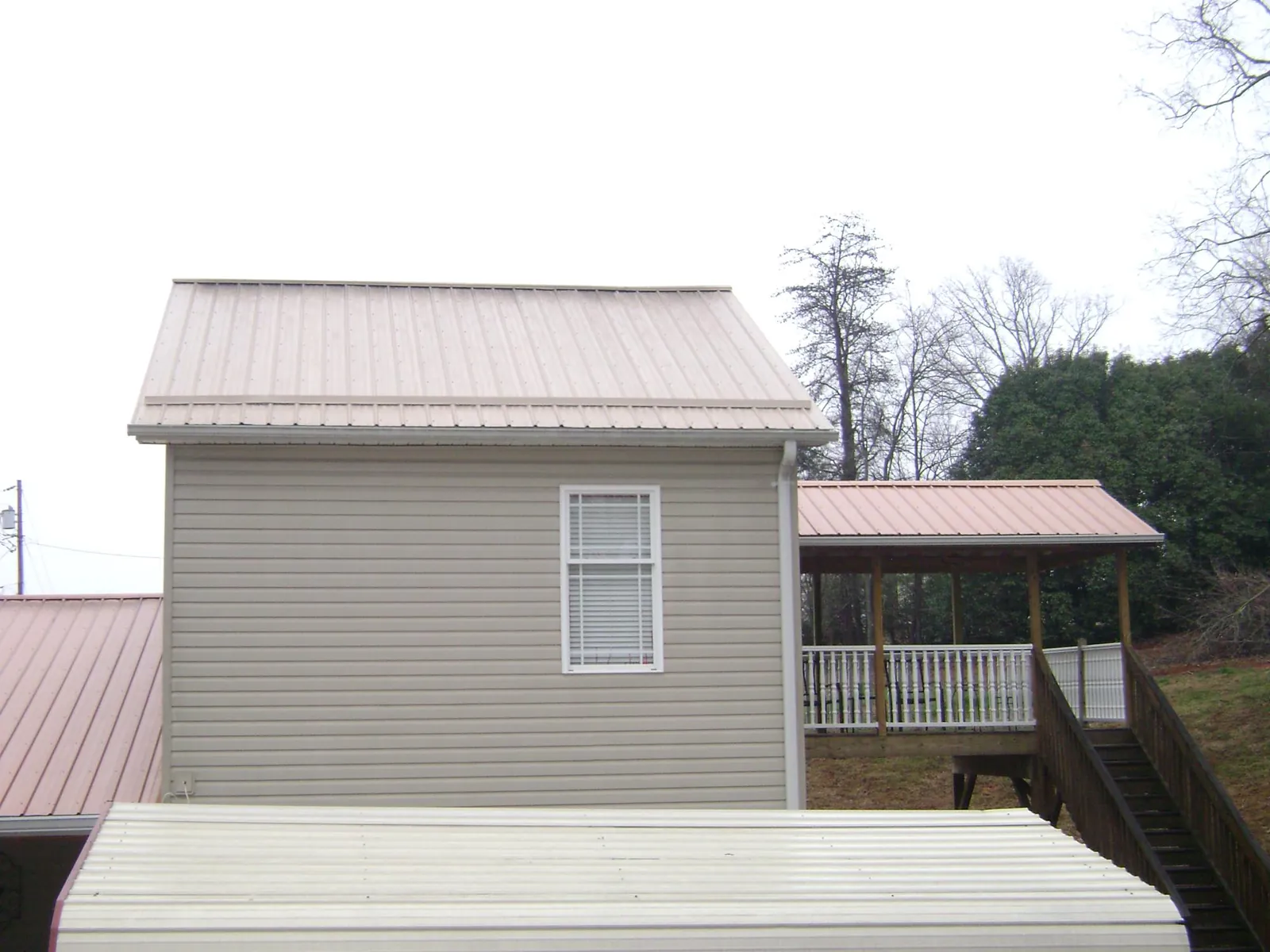 Tan metal roofs on a two story addition and attached porch, from a Roof Replacement job in Fort Ransom